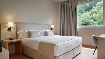 A hotel room with a bed, bedside tables, a desk, and a window with curtains.