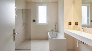 A modern bathroom with a glass shower enclosure, a freestanding bathtub, a large mirror, and a white vanity.