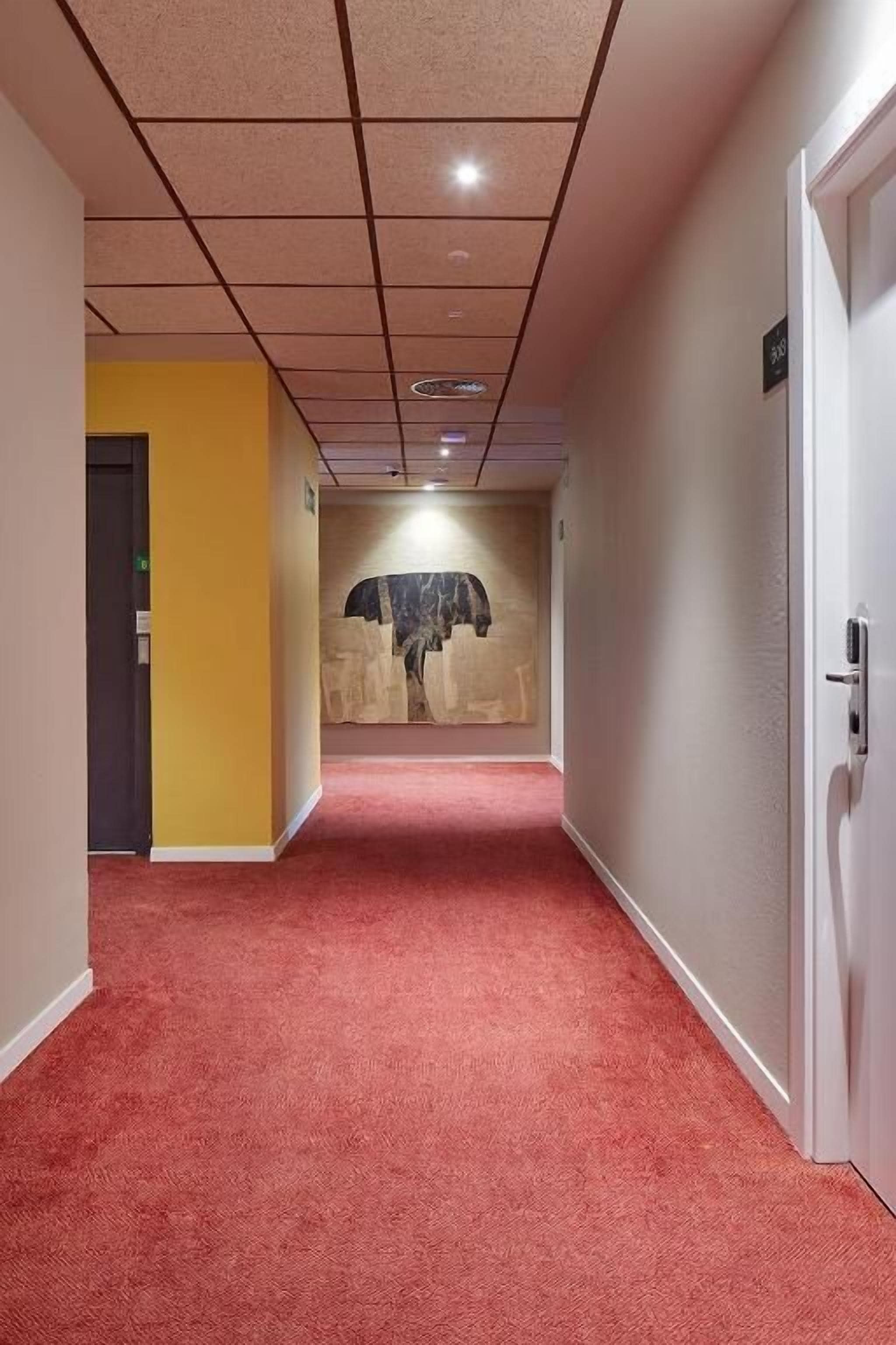 A hallway with a red carpet, a yellow wall, and a door on the left.