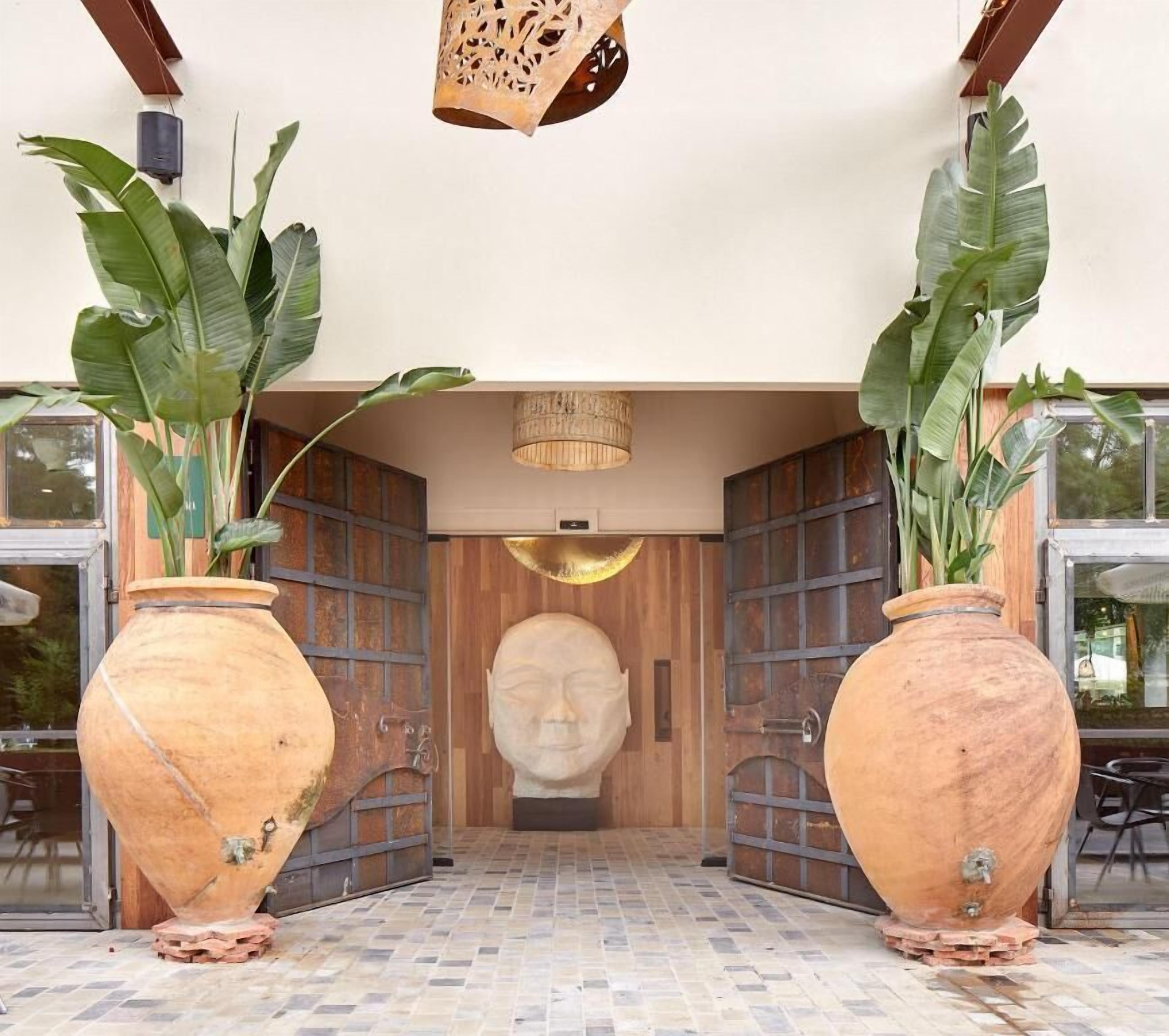 A building entrance with large vases, a wooden door, and a sculpture.