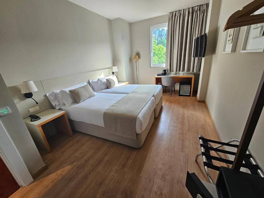 A hotel room with a double bed, a desk, a chair, a TV, and a window with curtains.