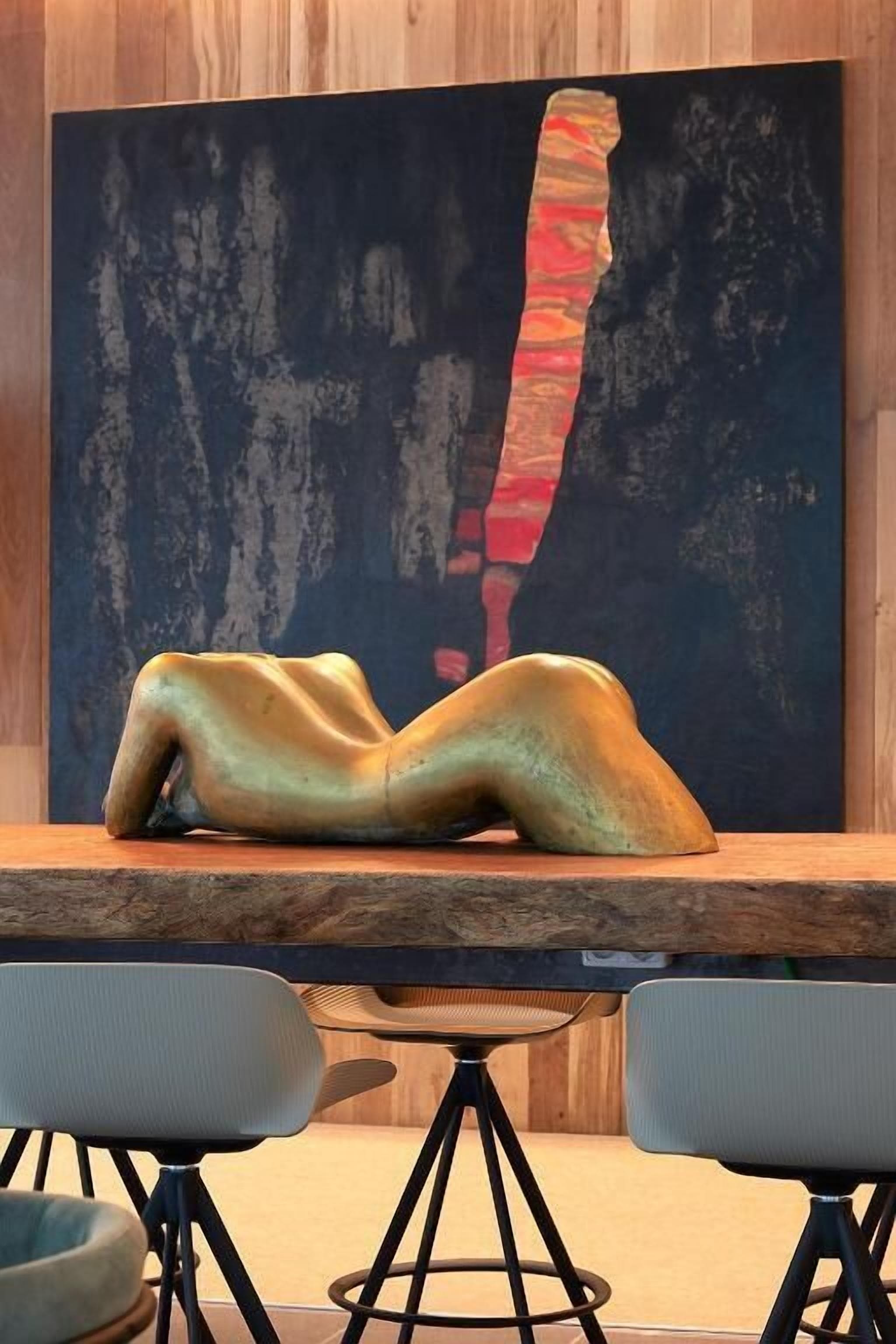 A modern dining area with a table and two chairs, a large abstract painting on the wall, and a sculpture on the table.