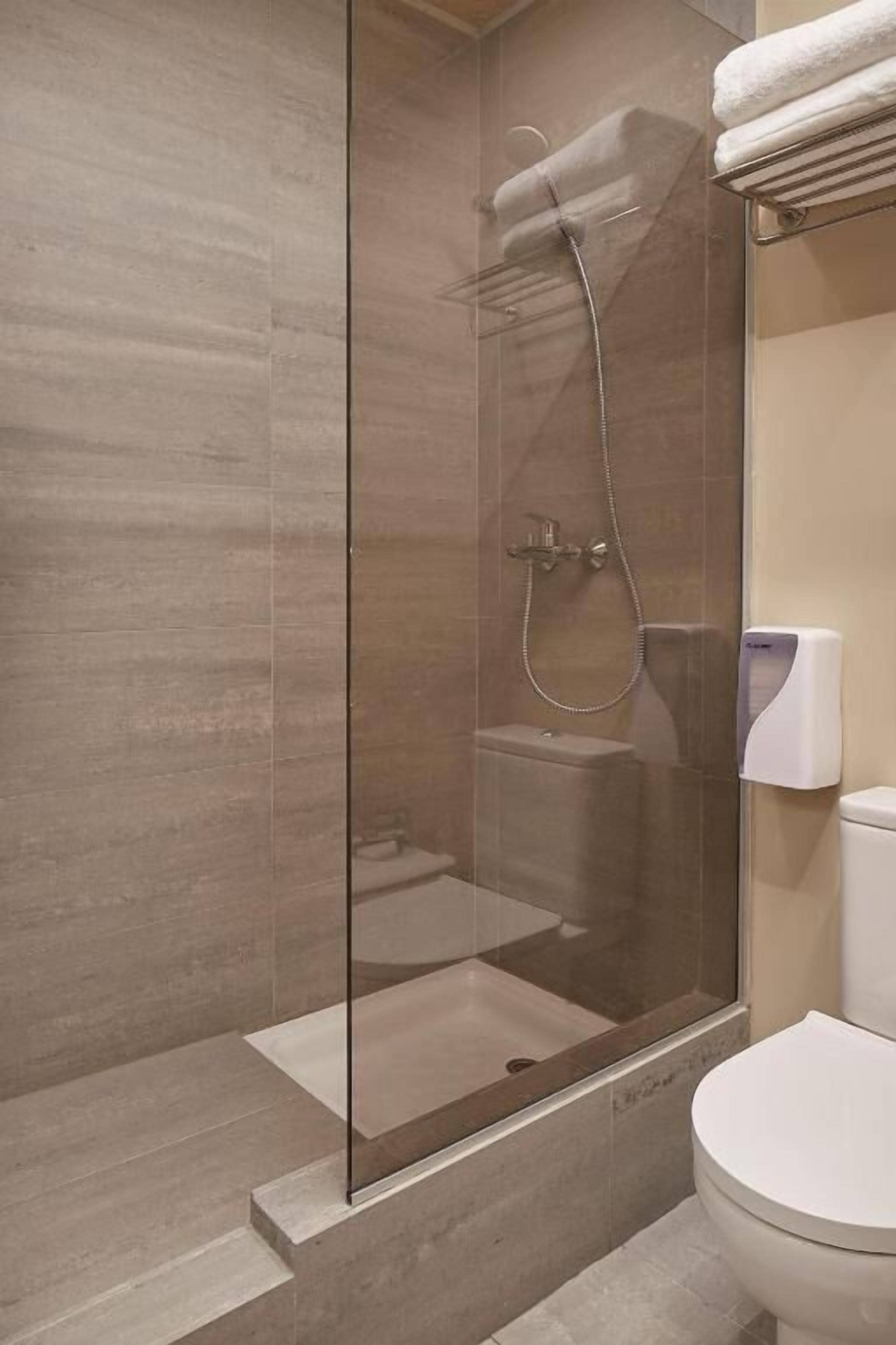 A modern bathroom with a glass-enclosed shower, a toilet, and a towel rack.