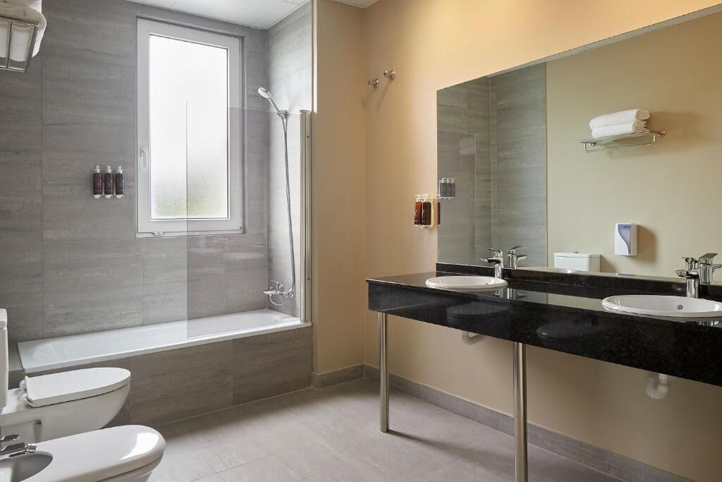 A modern bathroom with a bathtub, two sinks, and a large mirror.