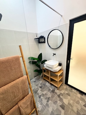 A bathroom with a white sink, a round mirror, a towel rack, a potted plant, and a door. - Stunning 1 Bedroom Villa in Seseh Area (Munggu)