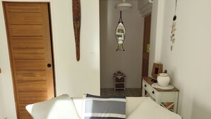 A room with a wooden door, a white sofa with striped cushions, a small table with a vase, and a mirror on the wall. - 2 ROOM APARTMENT NEAR THE SEA AND PINES OF JUAN-LES-PINS (Antibes)