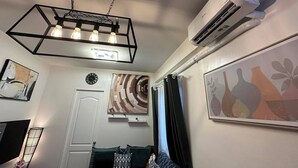 Una habitación con una lámpara de techo de diseño geométrico, un equipo de aire acondicionado, un reloj y obras de arte en las paredes.
