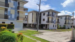Un moderno edificio residencial con varios balcones, un patio empedrado y abundante vegetación.