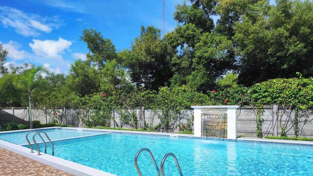 Una piscina rectangular con dos escaleras metálicas, rodeada por un suelo de baldosas y un muro de piedra bajo.