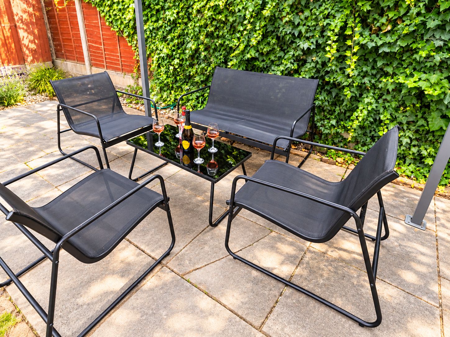 A patio with four black metal chairs and a table set with wine glasses and bottles.
