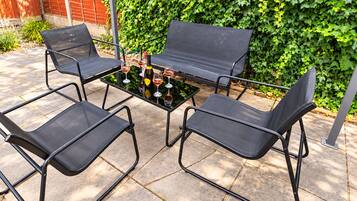 A patio with four black metal chairs and a table set with wine glasses and bottles.