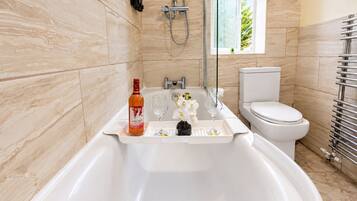 A modern bathroom with a bathtub, toilet, and a window with a view of greenery.