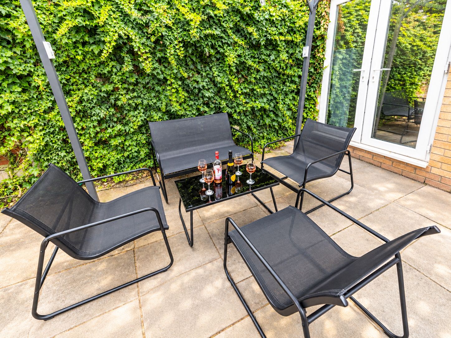 A patio with a table and four chairs, surrounded by a green hedge.