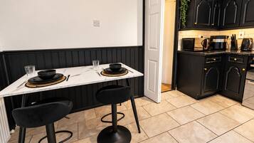 A modern kitchen with black cabinetry, a white countertop, and a dining area with a marble table and black chairs.