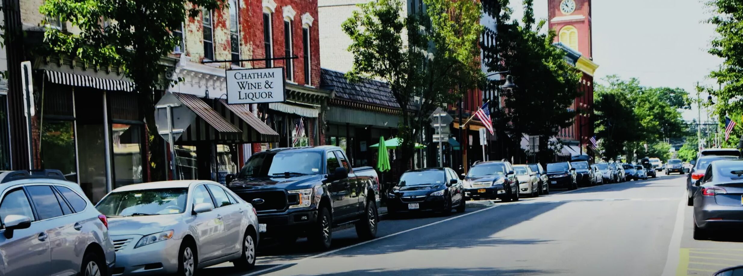 A street lined with parked cars and buildings, including a sign for Chatham Wine & Liquor.
