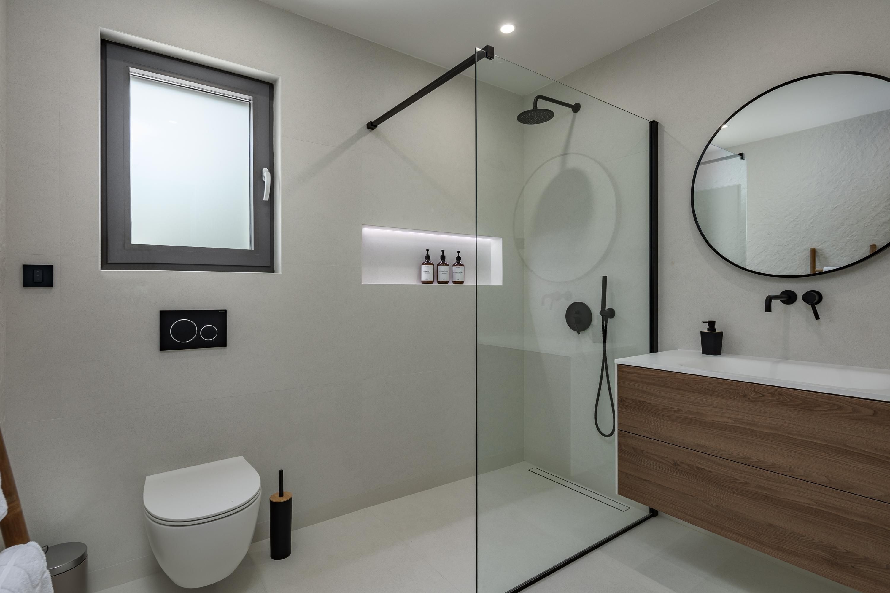 A modern bathroom with a glass-enclosed shower, a wooden vanity, a white toilet, and a mirror above the vanity.