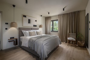 Une chambre moderne avec un grand lit, des tables de chevet, un luminaire suspendu, une fenêtre avec des rideaux et une plante.