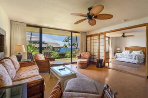 A spacious room with a large bed, a seating area with a coffee table, and a view of the ocean. - Ground Floor unit w/Ocean Views - Makahuena 2104 (Koloa)