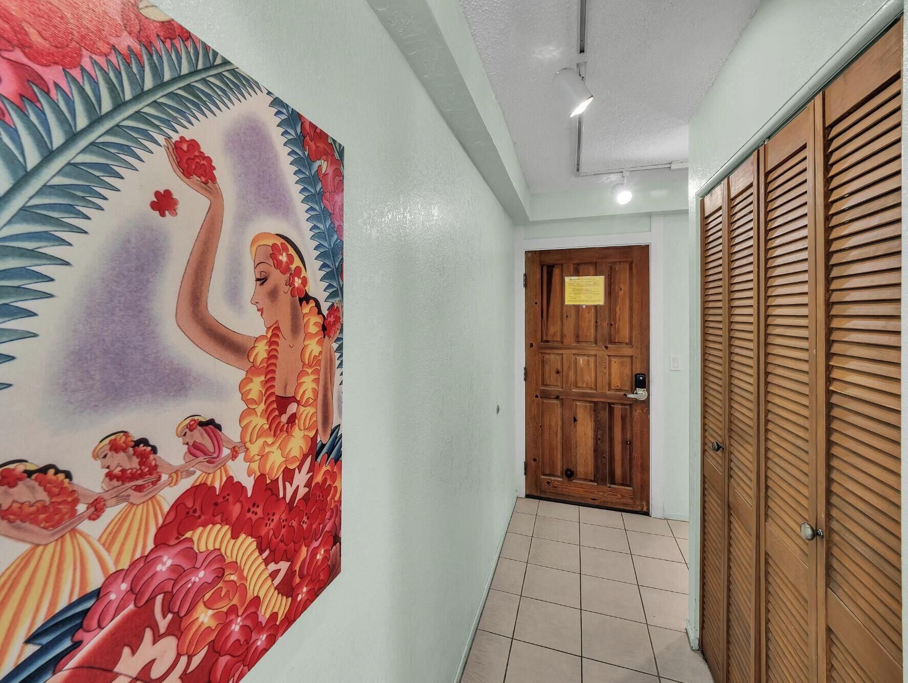 Un couloir avec une porte en bois, un mur orné d’une fresque florale et un sol carrelé.