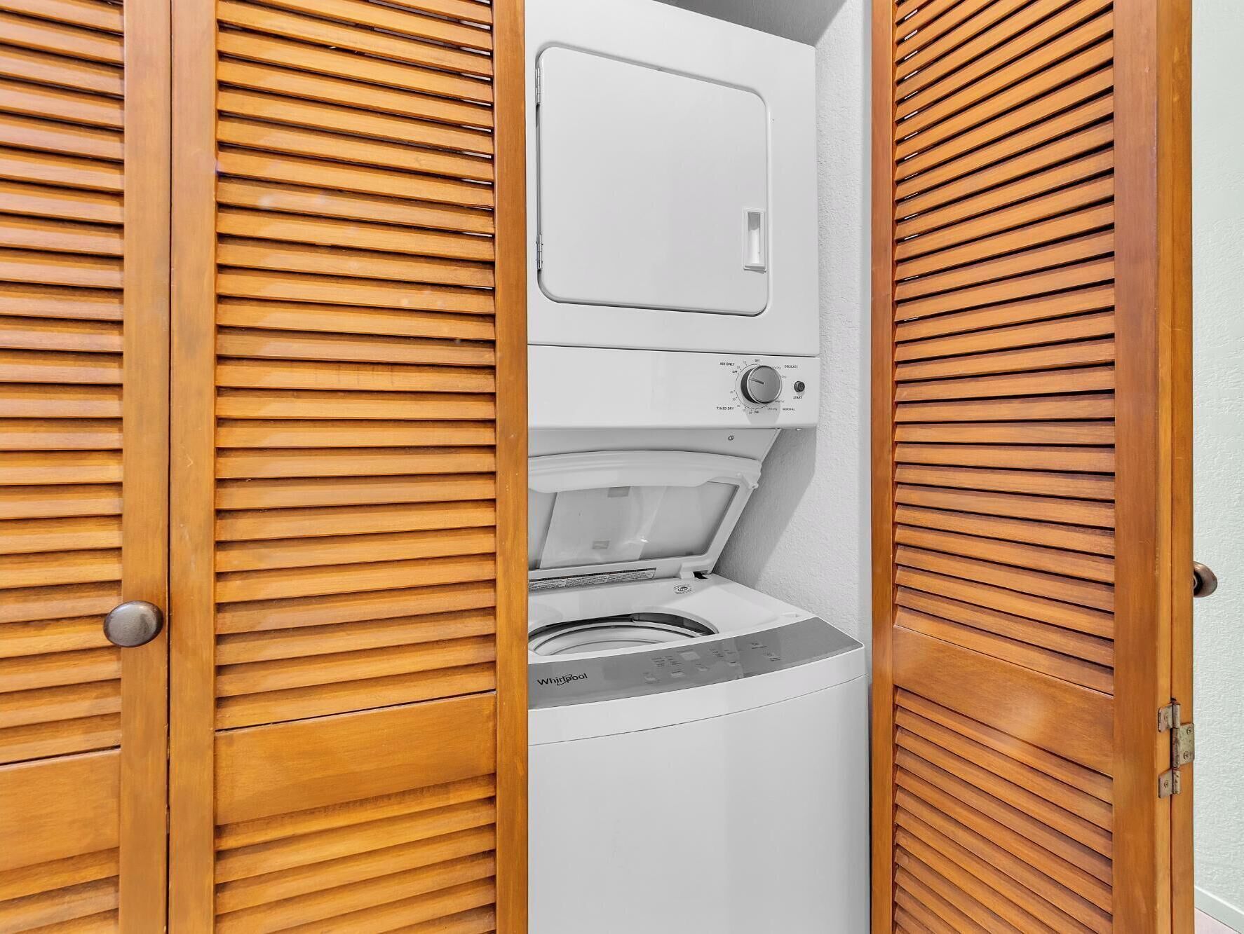 A compact, modern laundry room with a front-loading washer and dryer, enclosed by wooden louvered doors.