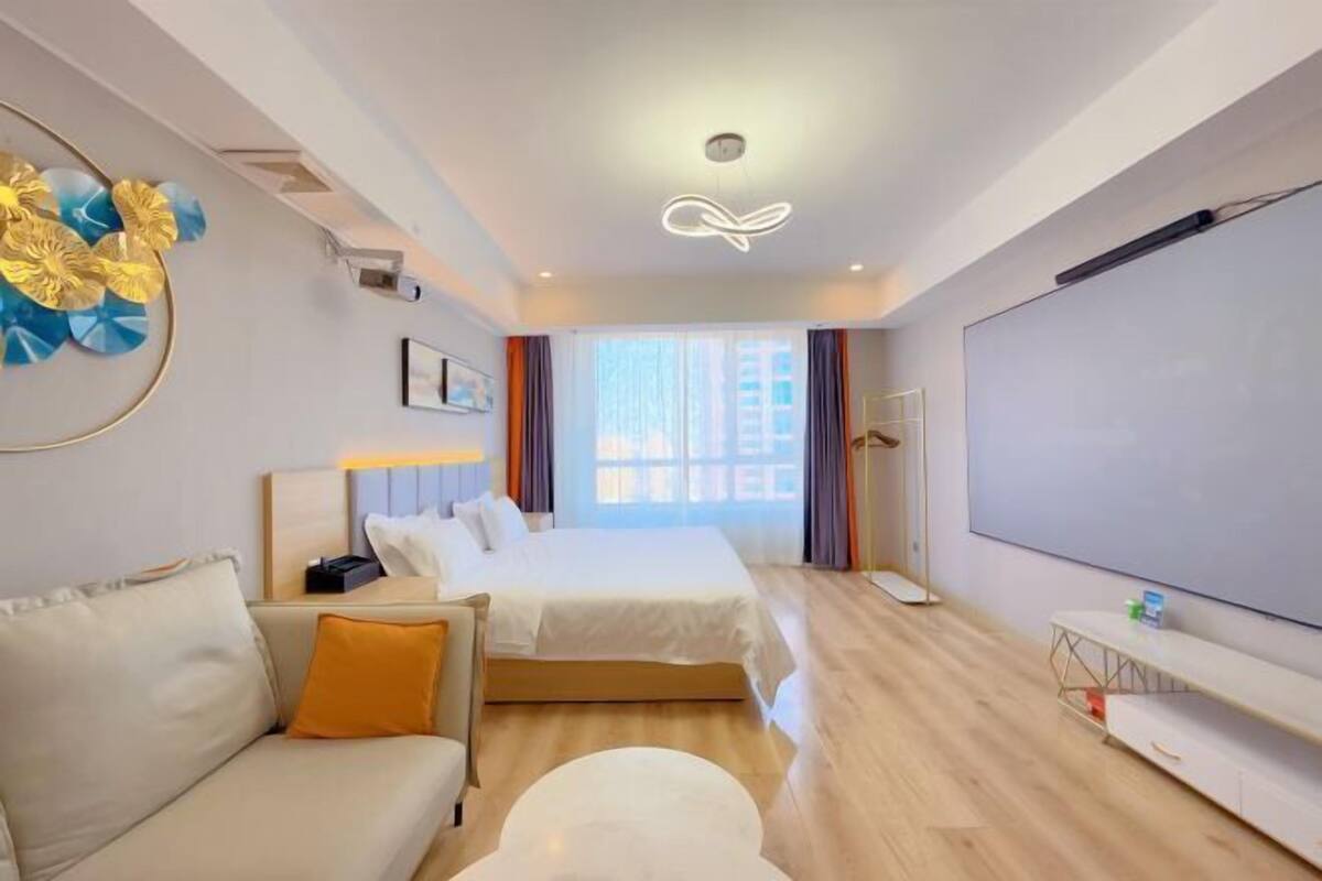 A hotel room with a bed, a sofa, a TV, and a large window.