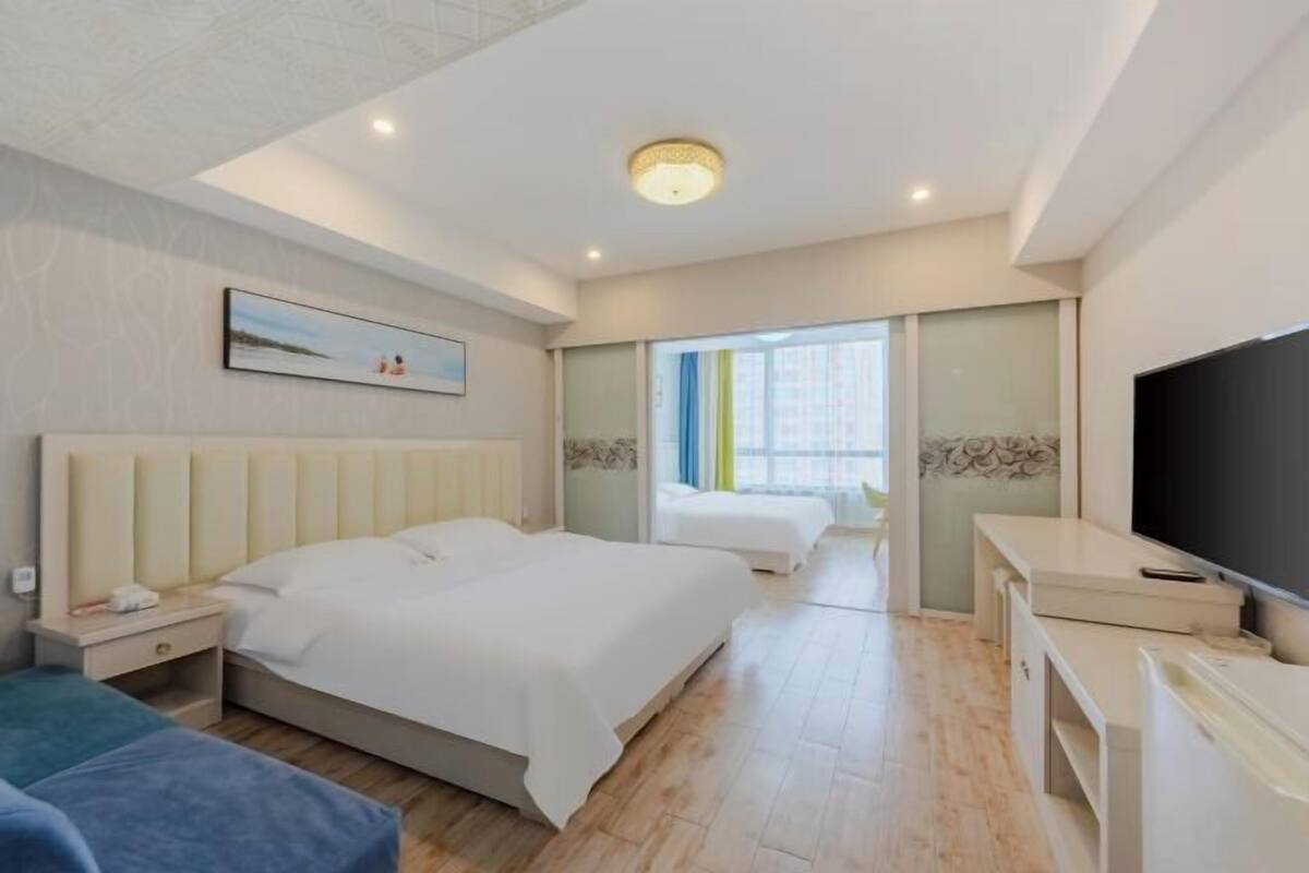 A hotel room with a bed, bedside tables, a TV, and a window with curtains.