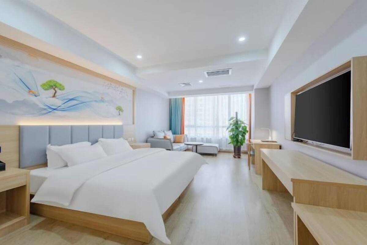 A modern hotel room with a large bed, a flat-screen TV, a desk, a sofa, and a painting on the wall.
