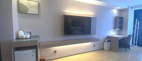 A modern living room with a flat-screen TV, a built-in coffee machine, and a small refrigerator.