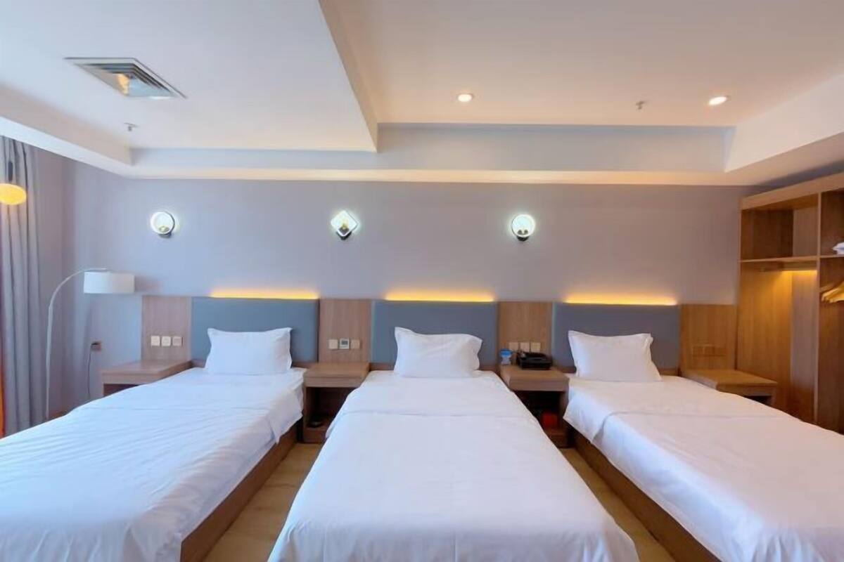 A hotel room with three single beds, a desk, a chair, and a wardrobe.