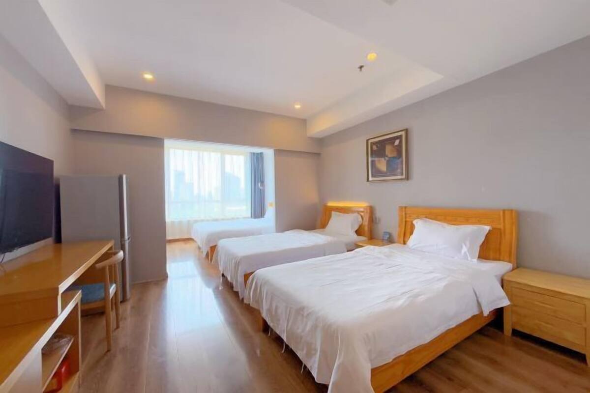 A hotel room with a wooden bed, a desk with a chair, a television, and a window with curtains.