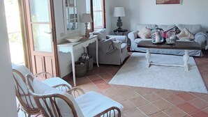 A cozy living room with a wooden ceiling, a white sofa, a dining table with chairs, and a large window. - Toskana Haus in Bigliolo mit Toller Aussicht, Garten, Sonne, in Flussnähe (Bigliolo)