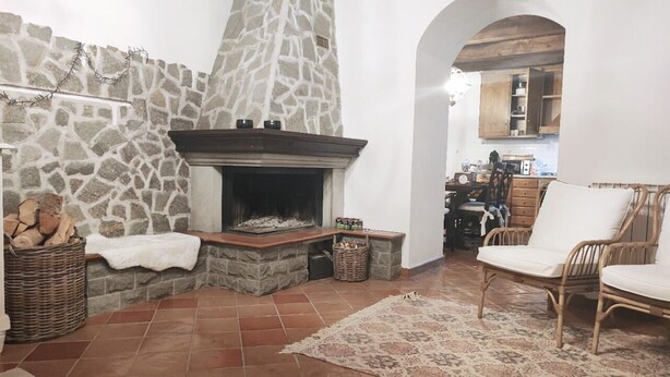 A cozy living room with a stone fireplace, wicker furniture, and a tiled floor. - Toskana Haus in Bigliolo mit Toller Aussicht, Garten, Sonne, in Flussnähe (Bigliolo)
