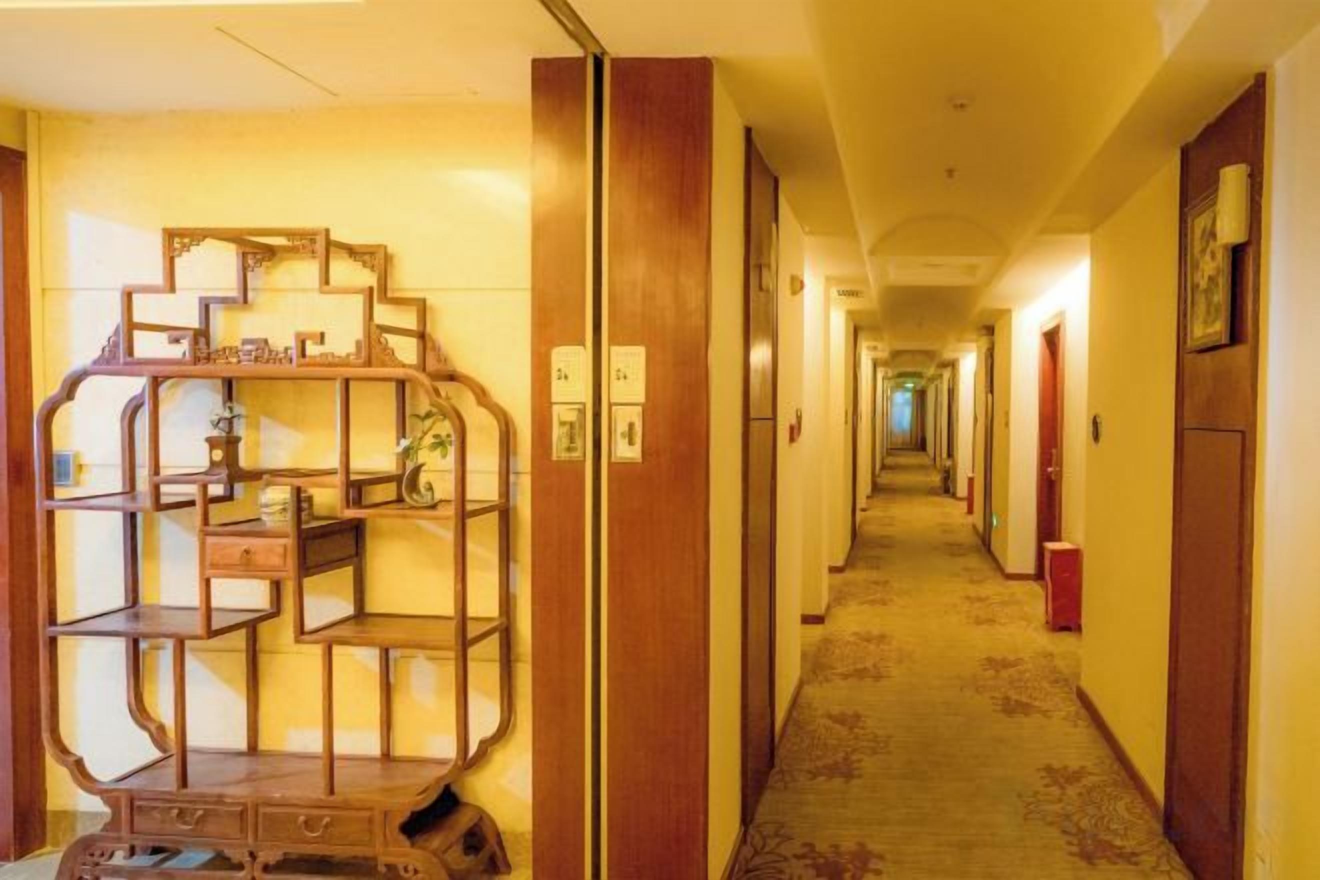 Corredor de hotel com prateleira de madeira, piso coberto por carpete e portas que dão para outros quartos.