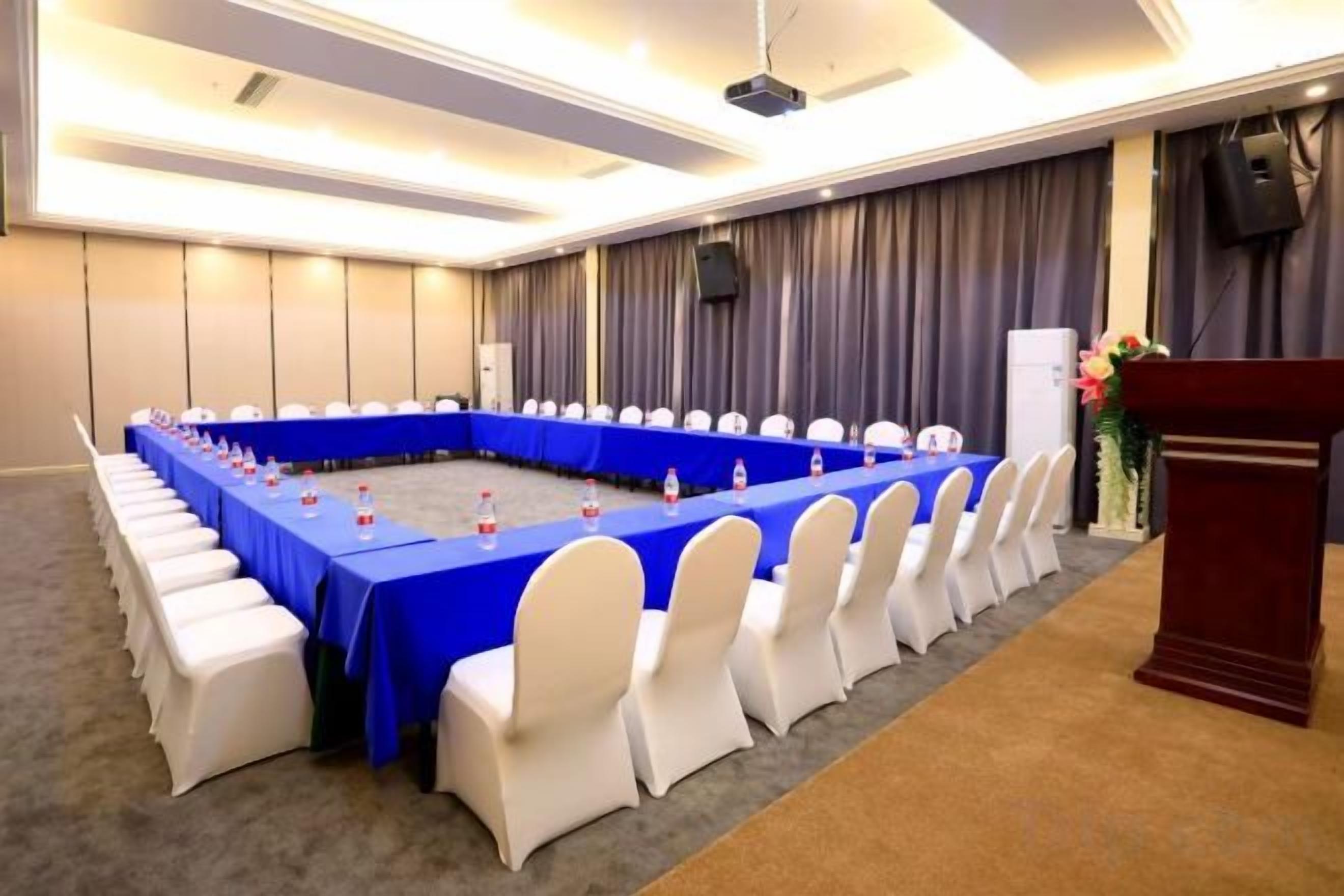 Uma sala de conferências com uma mesa comprida, cadeiras brancas e um pódio.