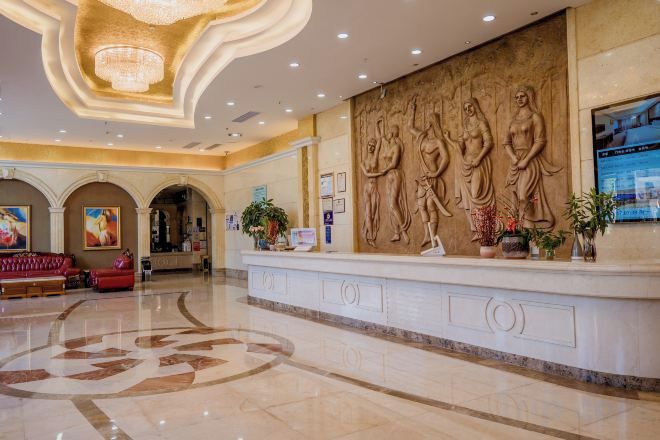 Vestíbulo de hotel con mostrador de recepción, una lámpara de araña grande y un muro con relieves escultóricos.