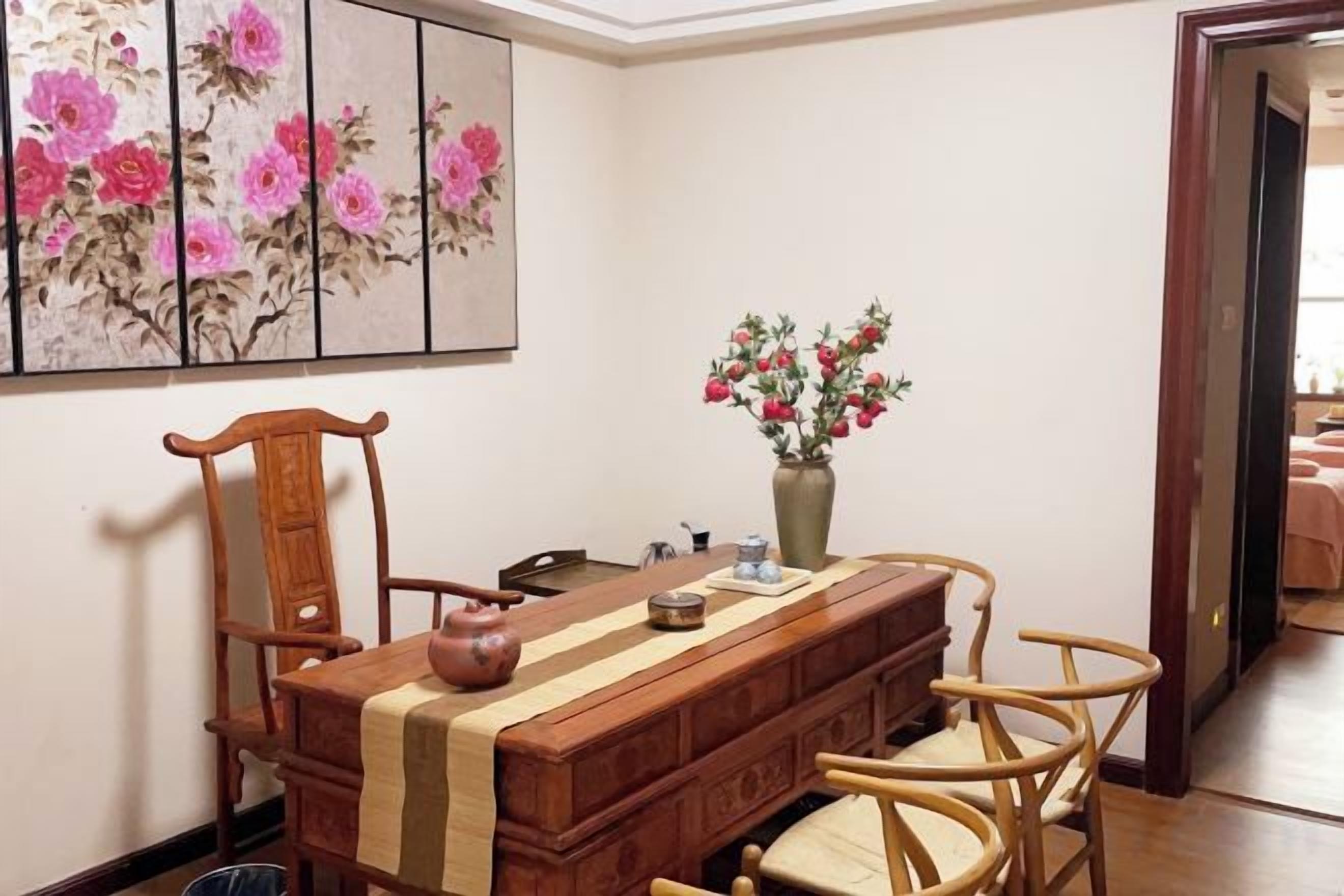 A dining area with a long wooden table, chairs, a vase with flowers, and a painting on the wall.