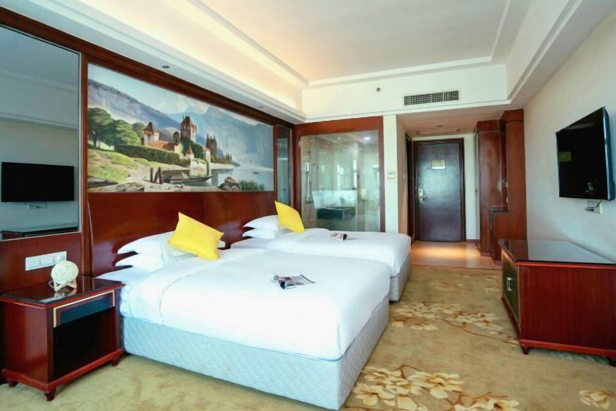 A hotel room with two beds, a large painting, a television, and a wooden dresser.