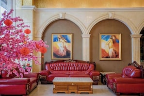 A lobby with a red leather sofa set, two paintings on the wall, and a large pink flowering plant. - Shenzhen Aitingbao Hotel (Shenzhen)