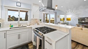 Une cuisine moderne dotée d’un îlot central, de meubles de rangement intégrés, d’une cuisinière et d’une grande fenêtre offrant une vue dégagée.
