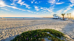 Une plage avec une tour de surveillance pour les sauveteurs, des voitures garées et des palmiers.