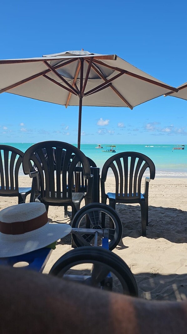 Playa con una fila de sillas de plástico negro y una sombrilla grande que da sombra.