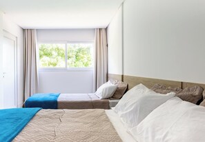Une chambre d’hôtel avec deux lits, une grande fenêtre avec des rideaux et une vue sur la verdure.