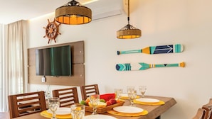 Een eetgedeelte met een houten tafel gedekt voor vier personen, een aan de muur bevestigde televisie en twee paddleboard decoraties.