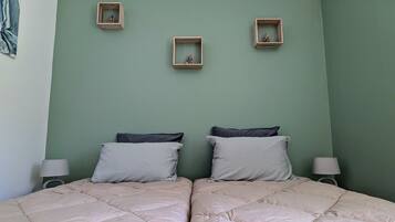 Une chambre avec deux lits, un mur vert et trois petites étagères en bois ornées de figurines.