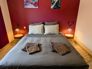 A neatly made bed with pillows and two folded towels, two bedside lamps, and artwork on the walls.