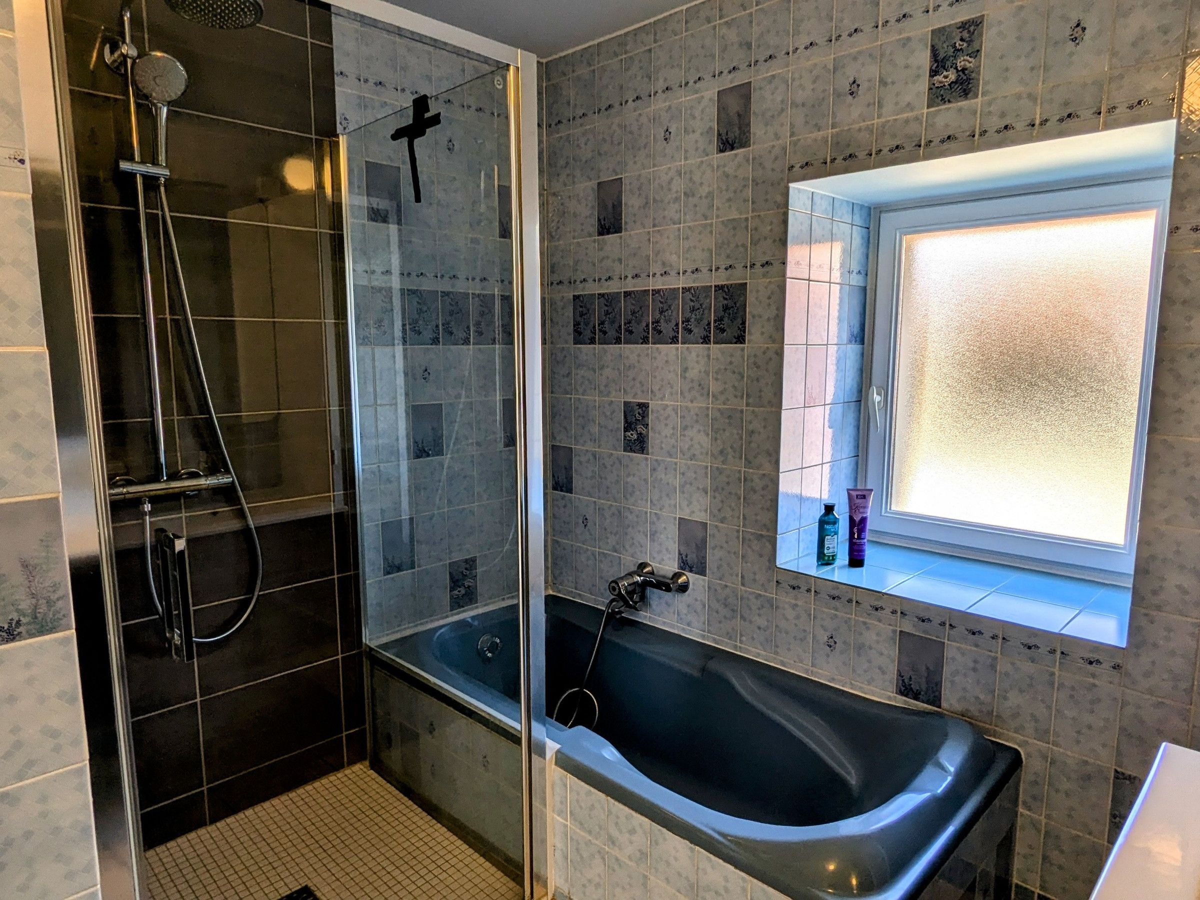 A modern bathroom with a glass-enclosed shower, a freestanding bathtub, and a window with frosted glass.
