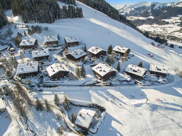 A snow-covered ski resort with multiple chalet-style buildings clustered together, surrounded by trees and a ski slope.