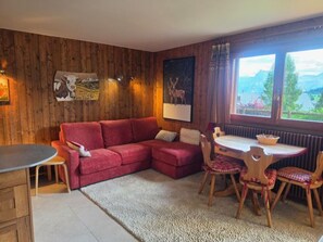 Una habitación acogedora con un sofá rojo, paredes de madera, una mesa de comedor con sillas y una ventana con vistas a zonas verdes.