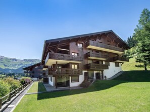 A multi-story chalet with balconies, set against a mountainous backdrop.