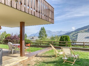 A wooden deck with outdoor furniture, a view of mountains, and a wooden fence.
